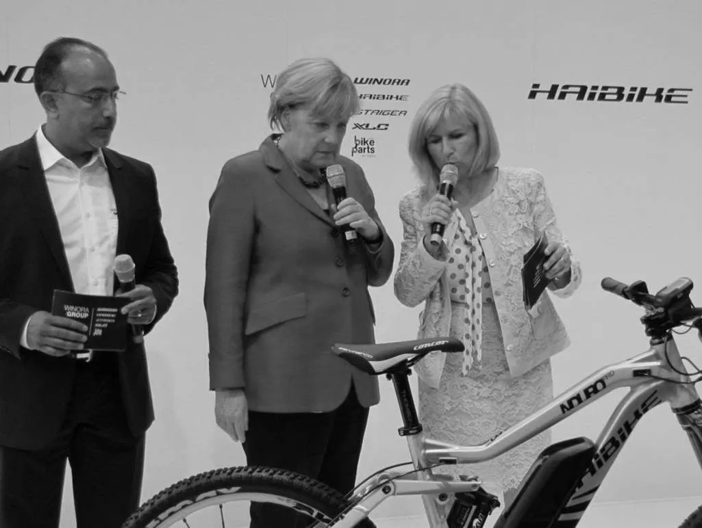 Schwarz-Weiß-Foto von drei Personen, die mit Mikrofonen auf einer Veranstaltung neben einem Fahrrad der Marke Haibike stehen.