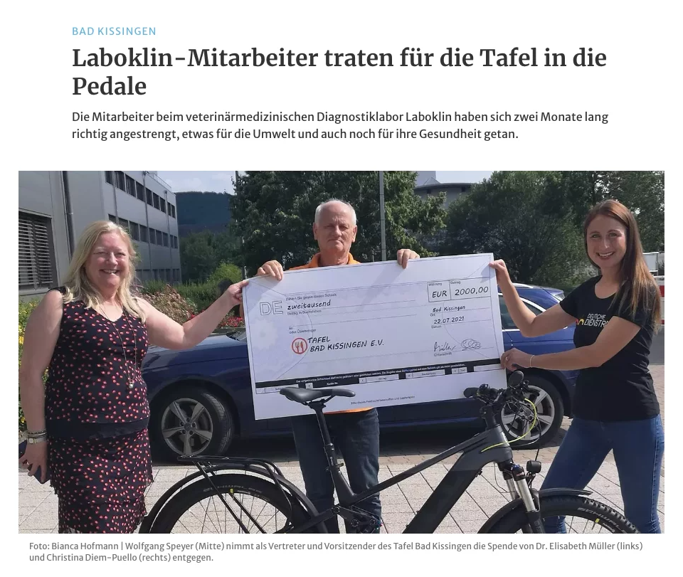 Ein Zeitungsartikel mit der Überschrift „Laboklin-Mitarbeiter traten für die Tafel in die Pedale“. Im Bild sind drei Personen zu sehen, die einen großen symbolischen Scheck über 2000 Euro halten. Links steht eine Frau, in der Mitte ein Mann, und rechts eine Frau in einem „Deutsche Dienstrad“-Shirt, vor einem Fahrrad.