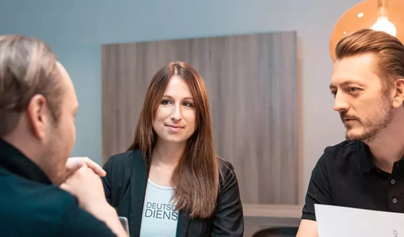 Drei Personen sitzen zusammen und unterhalten sich, die Frau in der Mitte trägt ein „Deutsche Dienstrad“-Shirt.